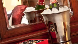 A room with a wooden bed, a mirror reflecting the room, and a minibar with champagne bottles and ice. - The Firgarth - Adults Only (Windermere)