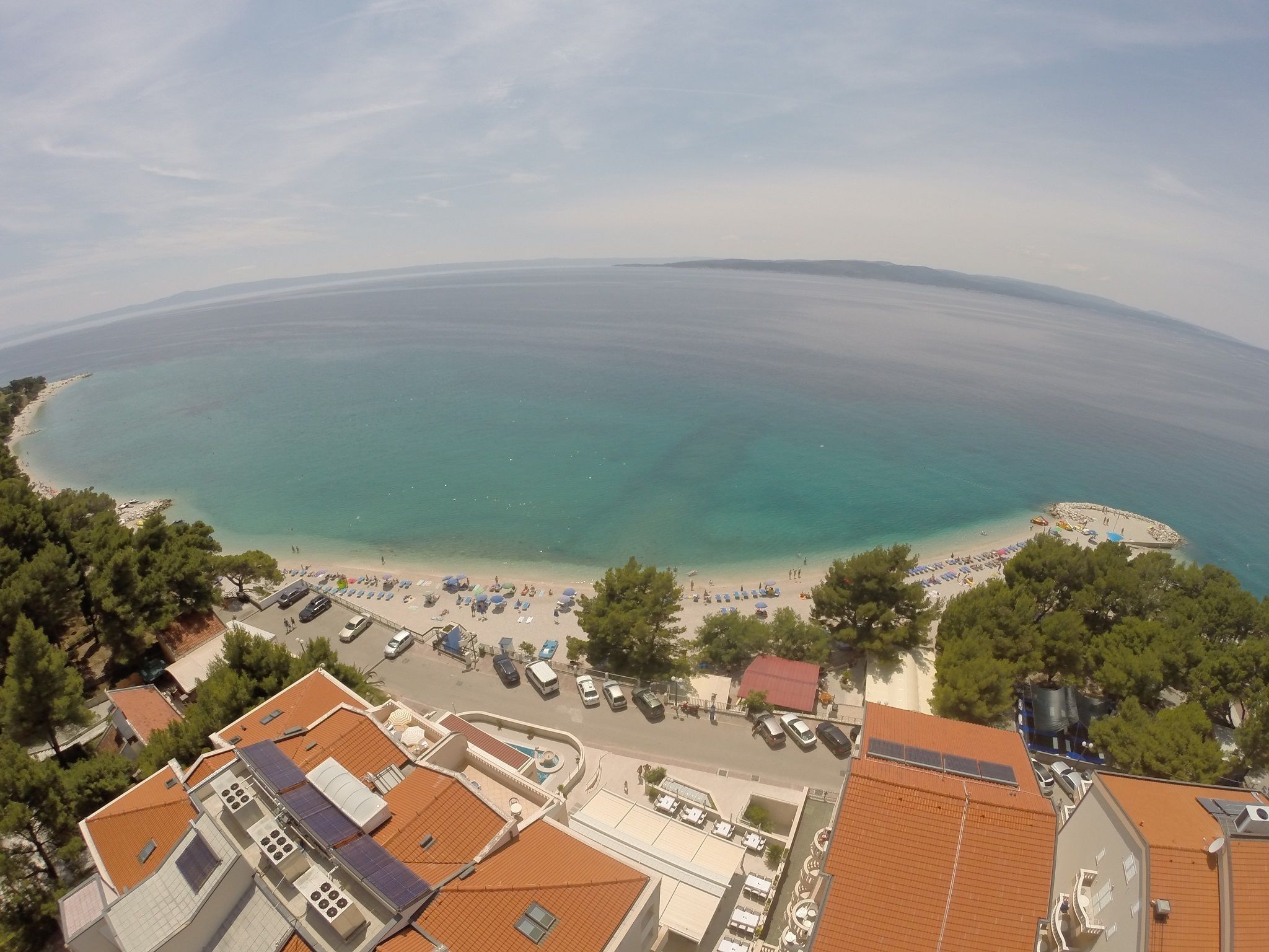 Une ville côtière avec une plage, des bâtiments aux toits recouverts de tuiles rouges et des voitures garées.