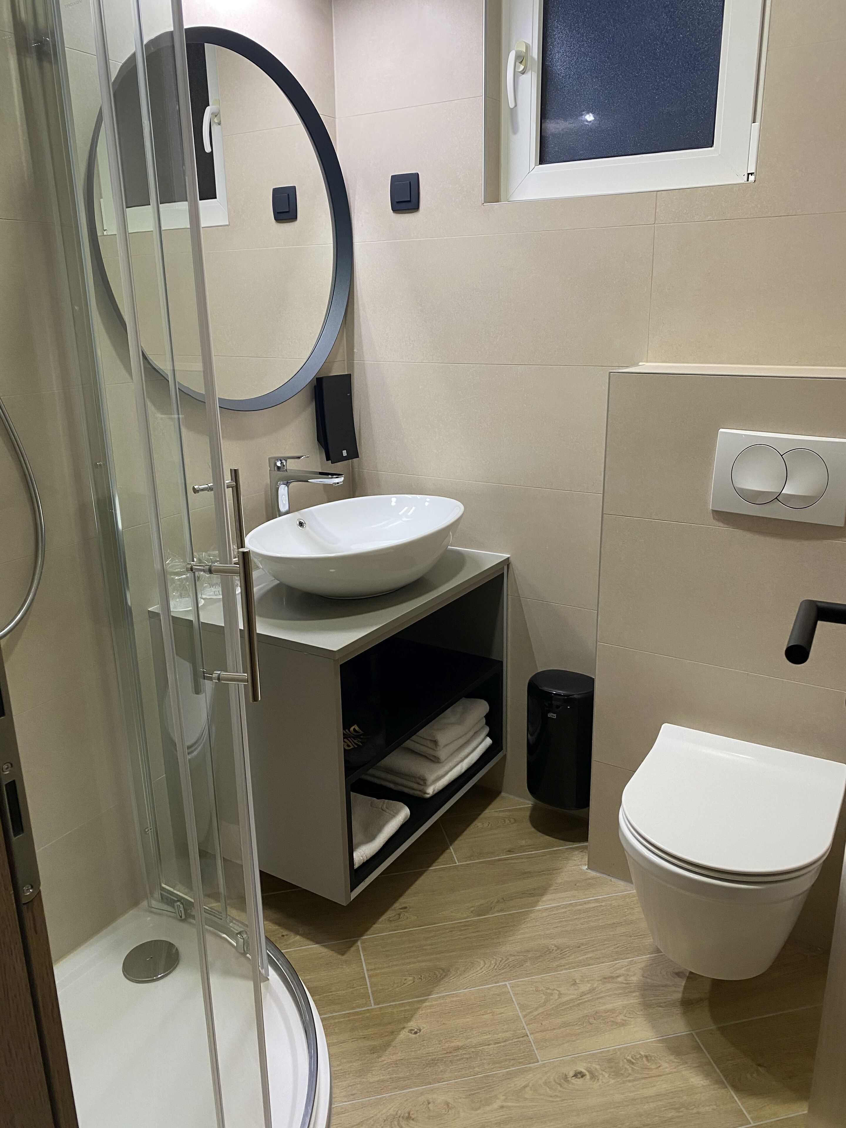 A modern bathroom with a glass-enclosed shower, a white sink, a toilet, and a small window.