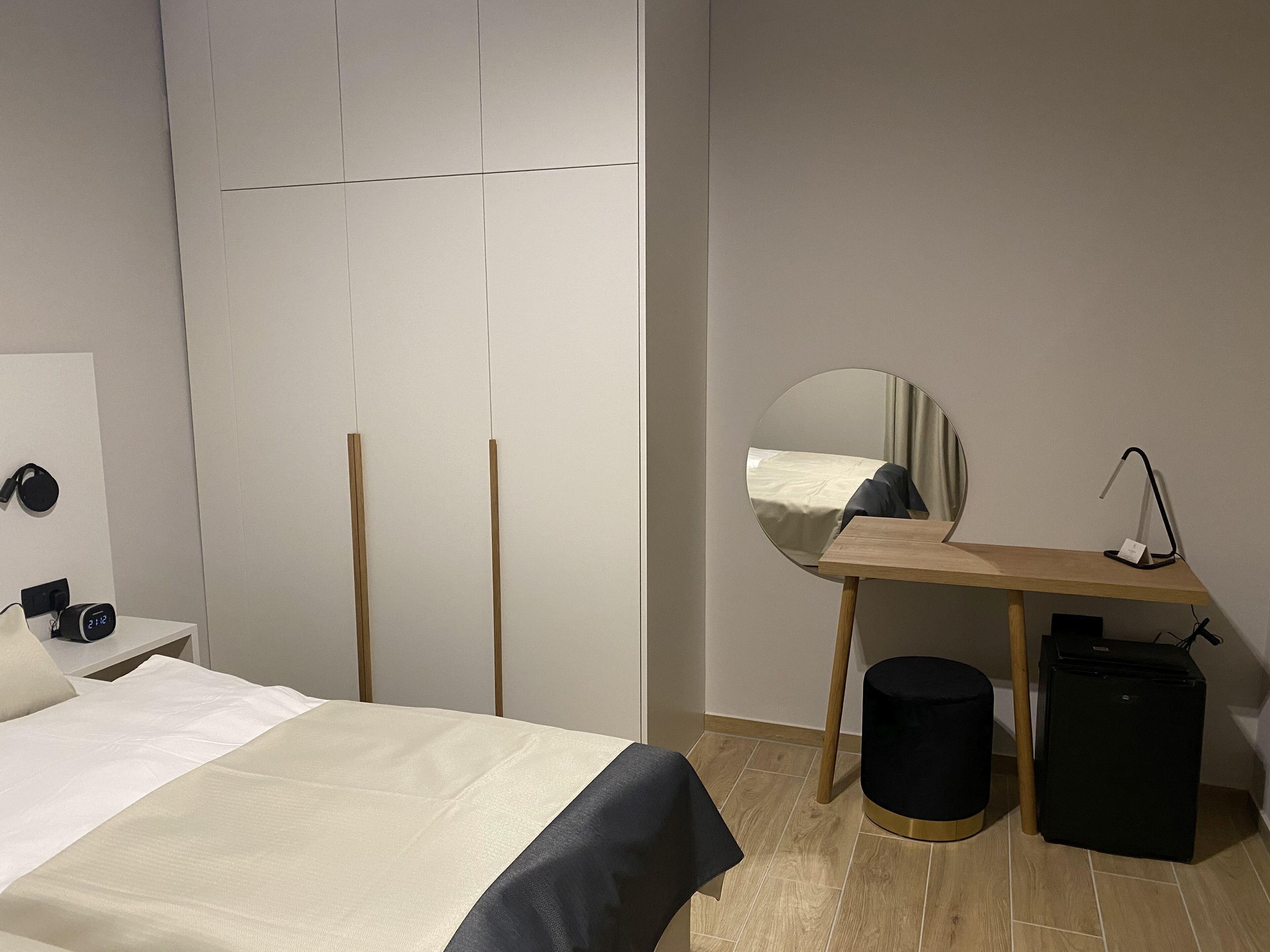 Une chambre d’hôtel moderne équipée d’un lit, d’une table de chevet, d’un miroir, d’un bureau et d’une petite enceinte noire.