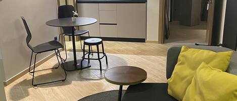 Un espacio habitable compacto con kitchenette, zona de comedor y área de descanso con sofá y cojines.