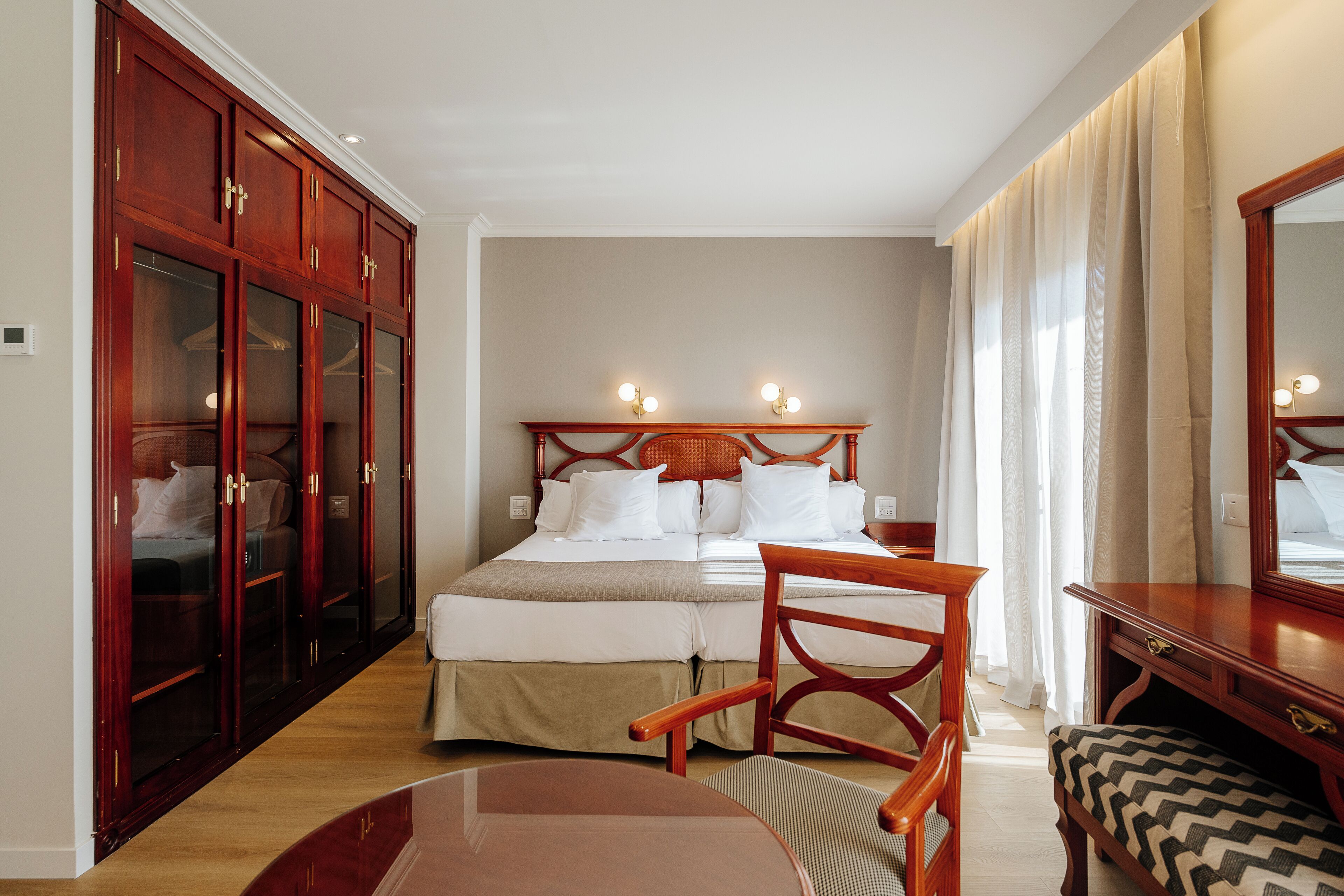 Una habitación de hotel con cama, armario de madera, escritorio y silla.