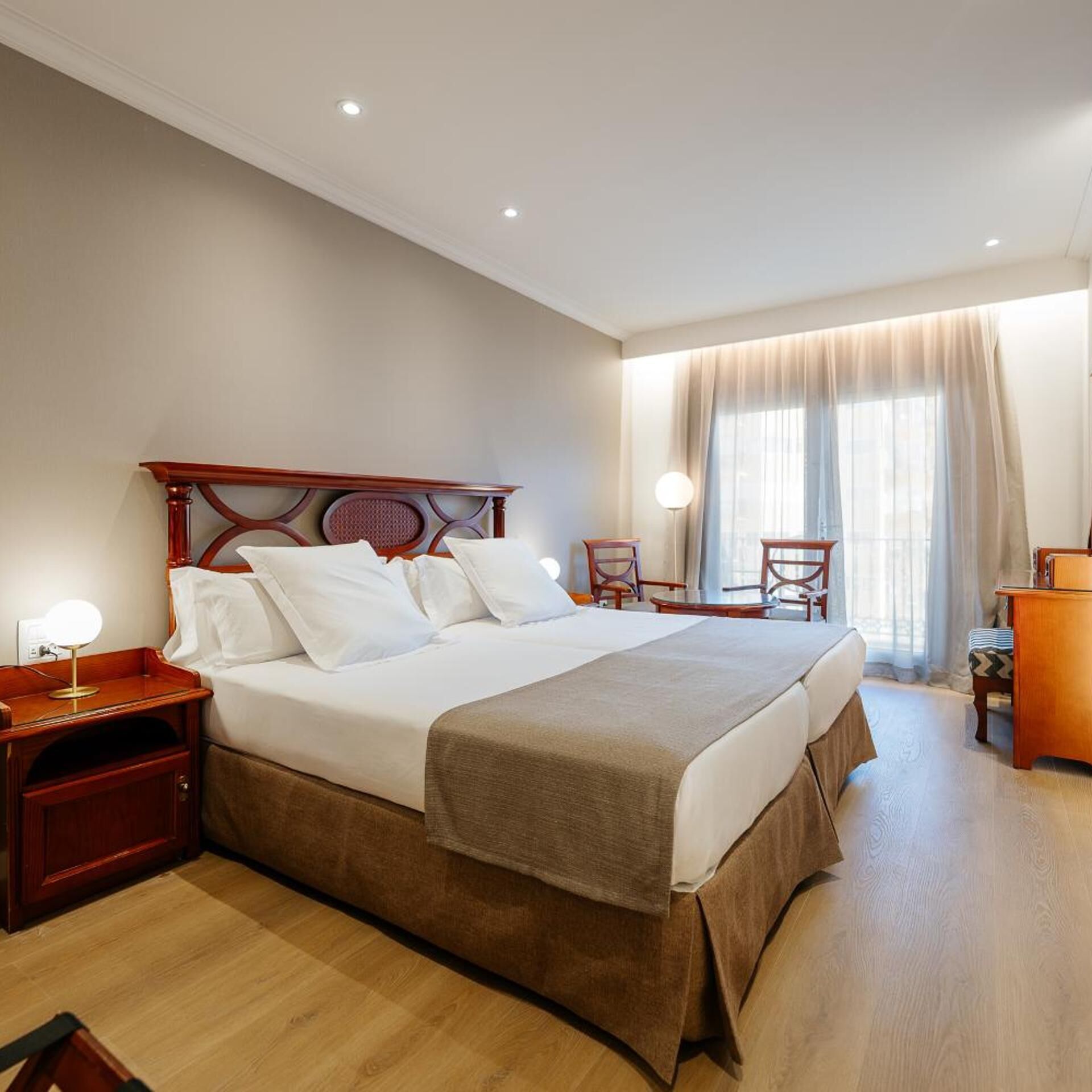 Una camera d'albergo con un letto grande, comodini, una scrivania, una sedia e una finestra con tende.