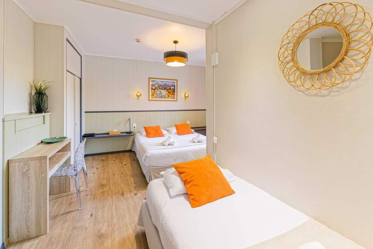 A hotel room with two beds, a desk, a chair, a mirror, and a picture on the wall.