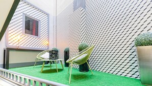 A modern outdoor seating area with two chairs, a small table, and decorative potted plants against a geometric wall. - Hôtel Côte Basque (Bayonne)