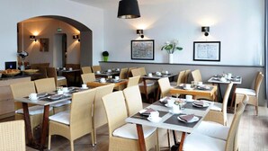 A modern restaurant with wicker chairs and tables, a kitchen area, and framed artwork on the walls. - Hôtel Côte Basque (Bayonne)