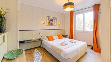 Une chambre d’hôtel avec un lit, un tableau, une fenêtre avec des rideaux, une plante et un bureau avec une chaise.