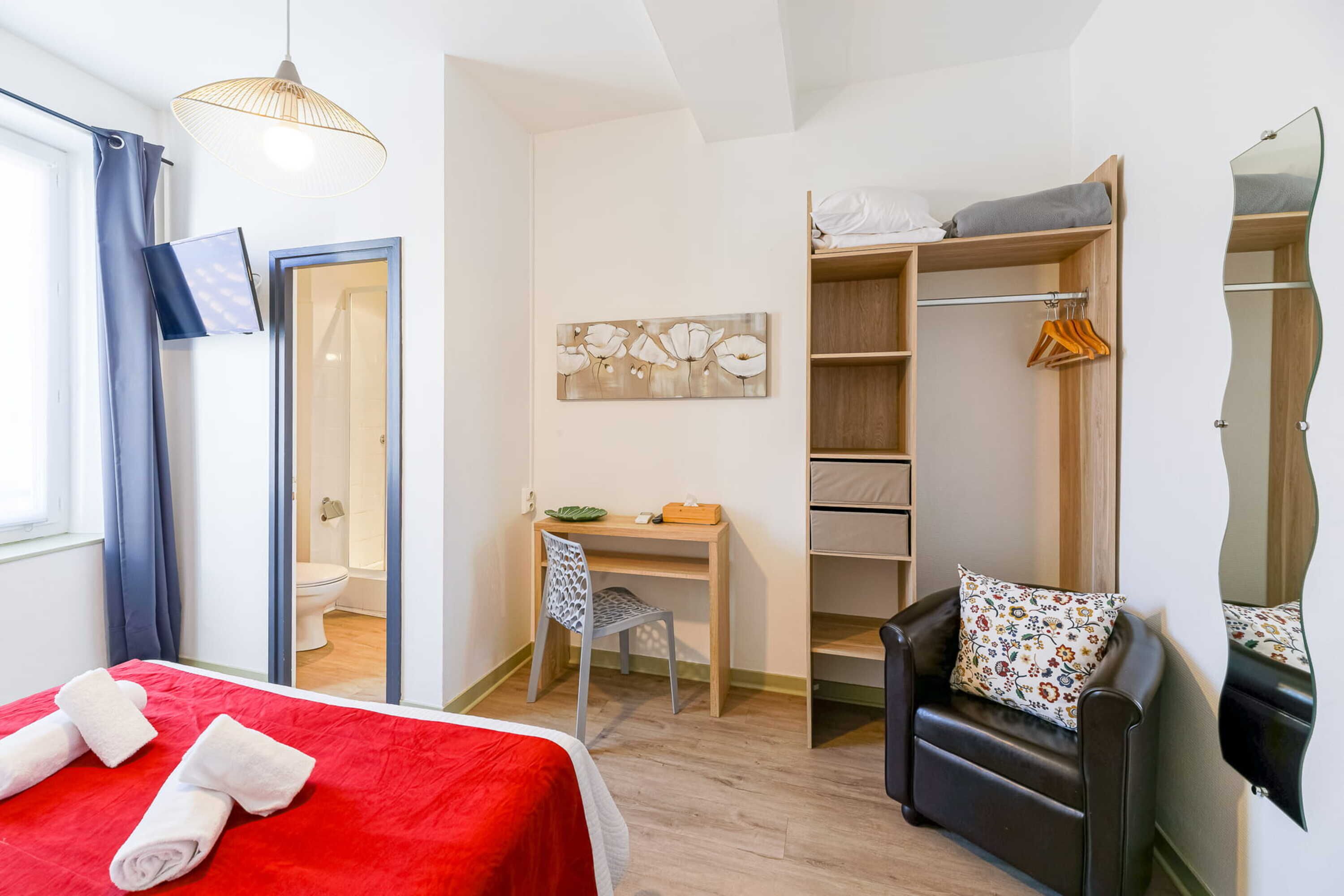 A hotel room with a bed, a desk, a chair, a wardrobe, and a mirror.