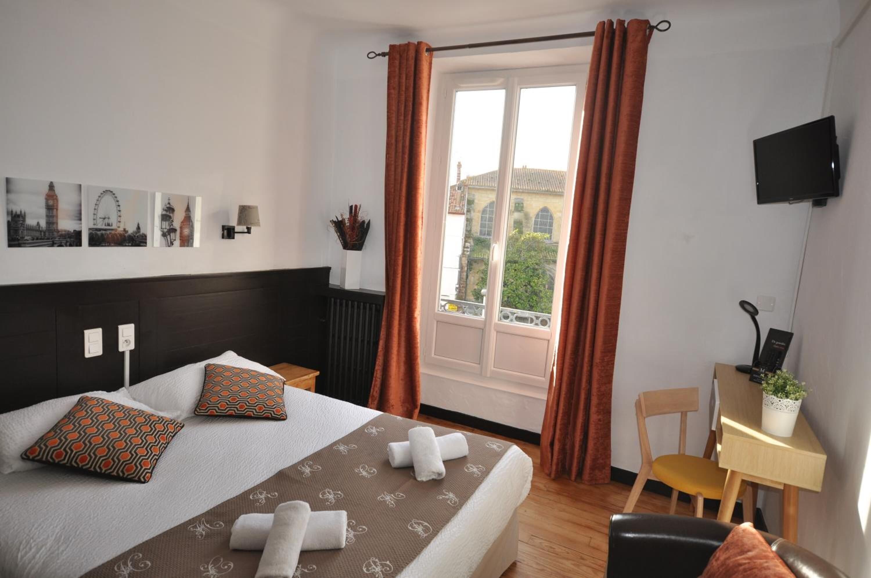 Habitació d'hotel amb llit, escriptori, cadira, televisió i finestra amb cortines.