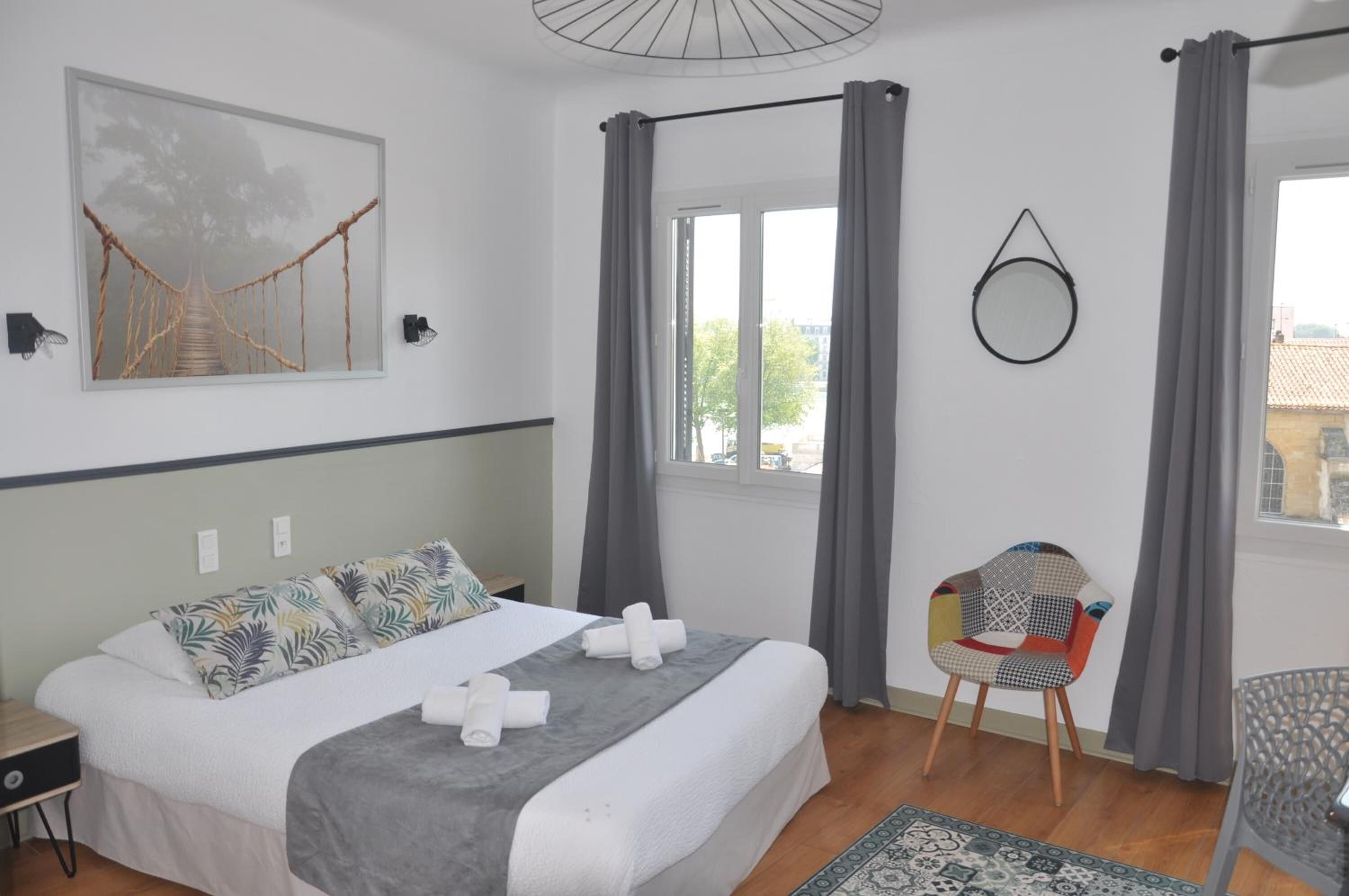 Un dormitorio con cama, una silla, un ventanal y una obra de arte colgada en la pared.