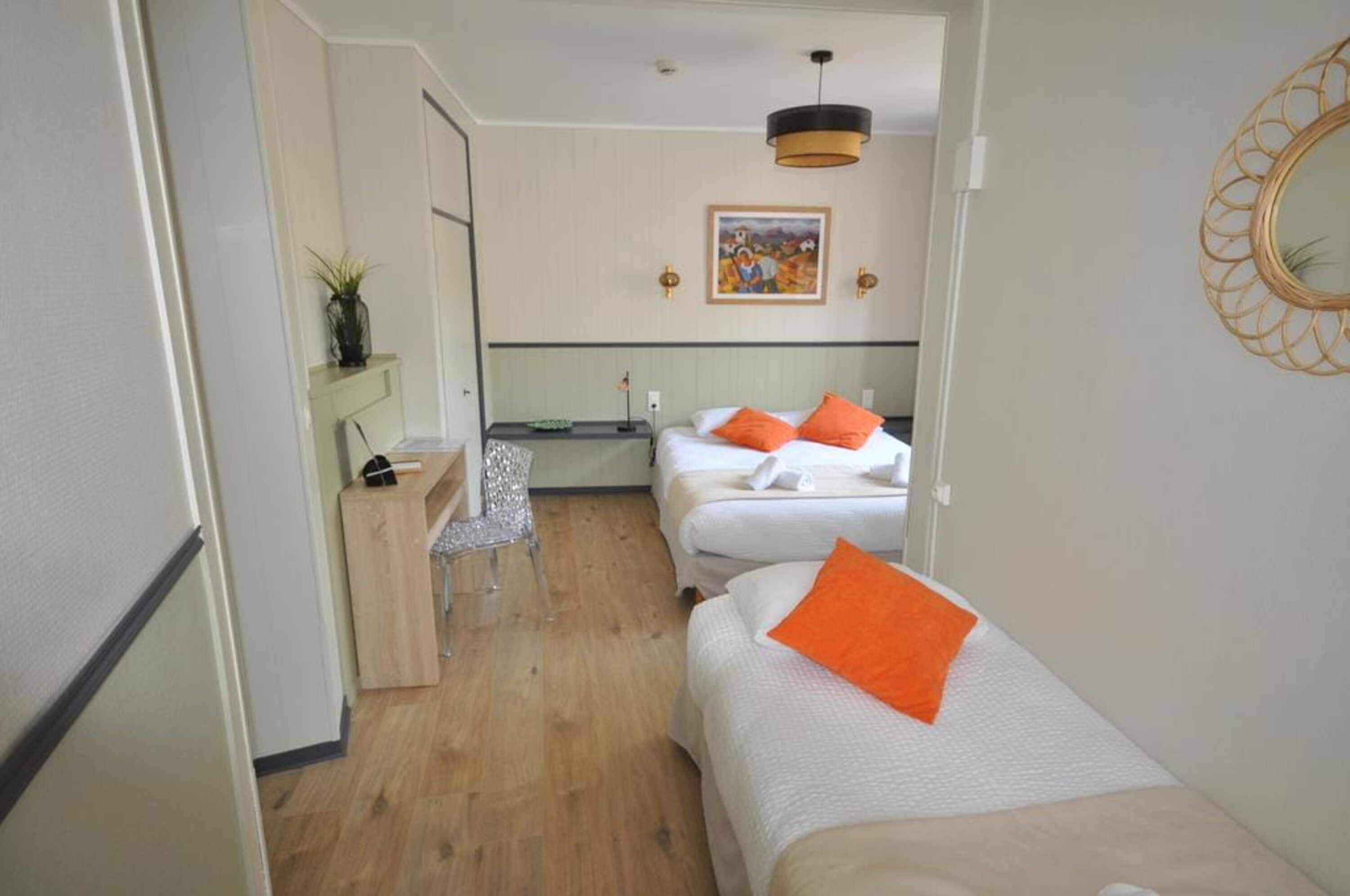 A hotel room with two beds, a desk, a chair, and a mirror.