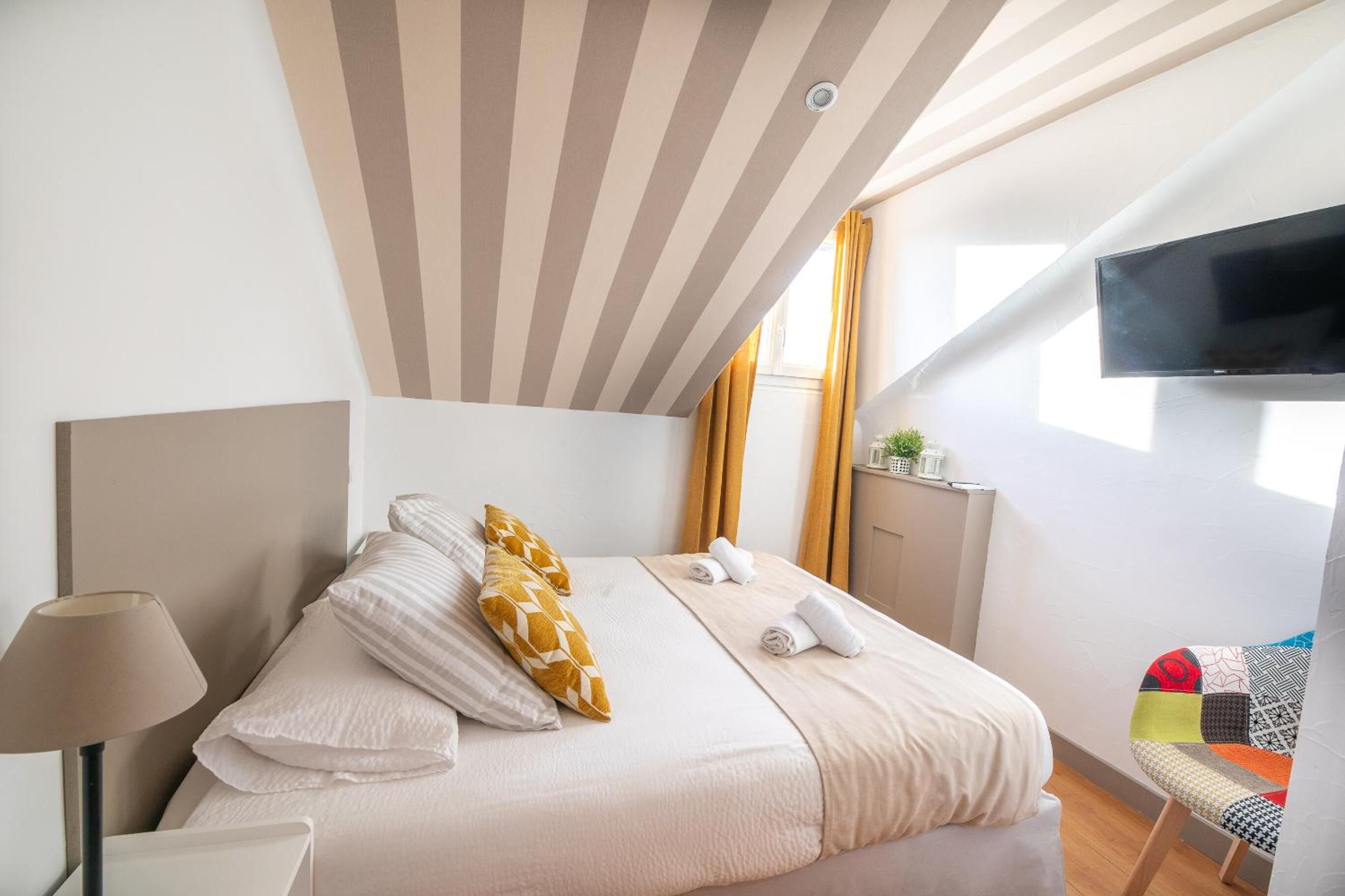 Une chambre d’hôtel moderne dotée d’un grand lit, d’un téléviseur à écran plat fixé au mur et d’une fenêtre avec des rideaux.