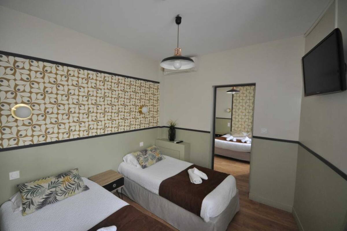 A hotel room with two single beds, a large mirror, a TV, and a patterned wall.