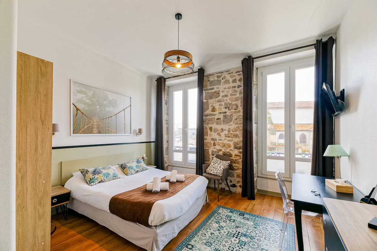 A bedroom with a bed, a chair, a desk, a lamp, and a view of the outside.