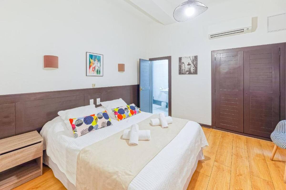 A hotel room with a bed, a wooden nightstand, a wardrobe, and a door leading to a bathroom.