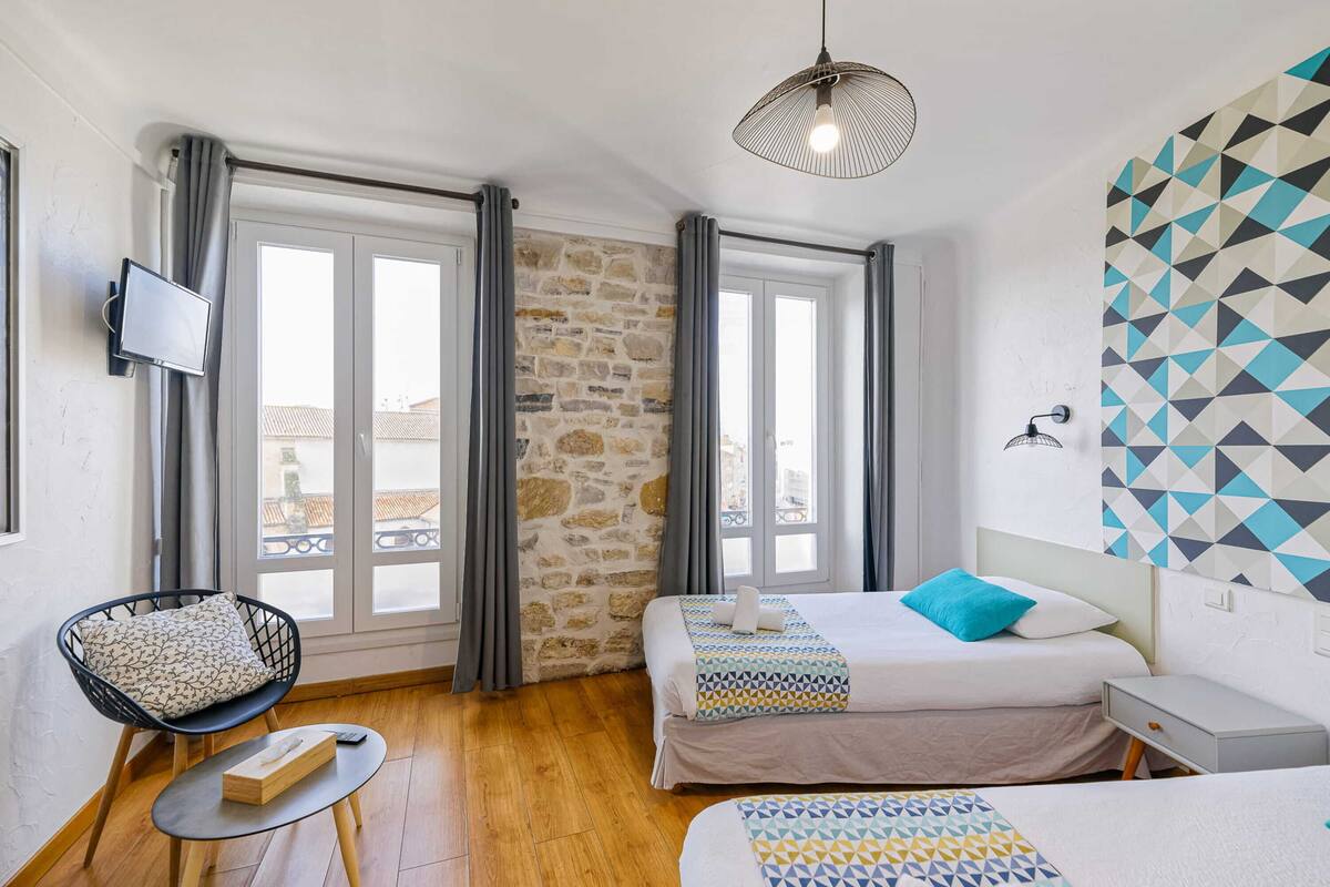 A hotel room with a stone wall, two beds with patterned bedding, a TV mounted on the wall, and a balcony view.