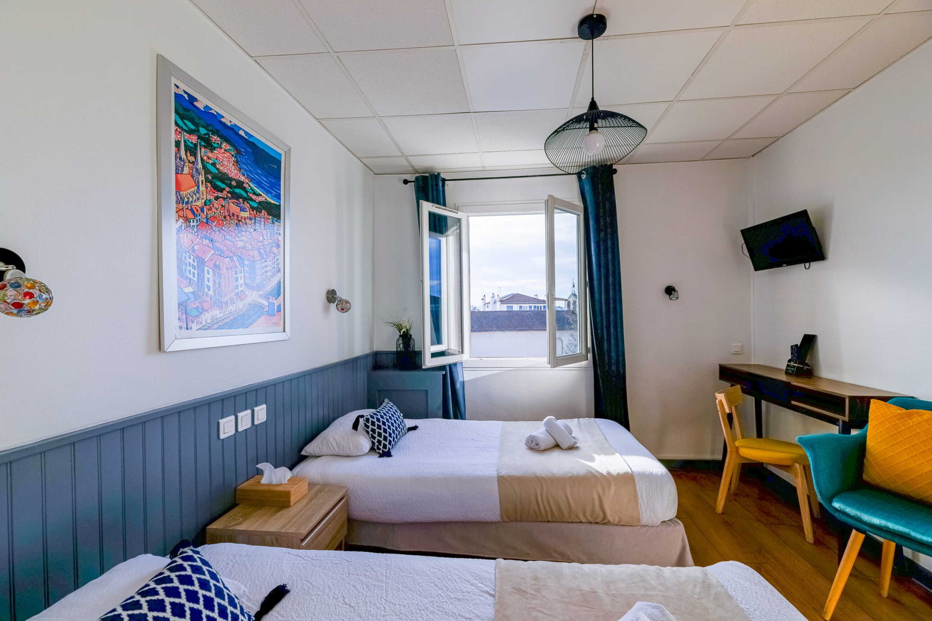 Una habitación de hotel con dos camas, un escritorio, un televisor y una ventana con cortinas.
