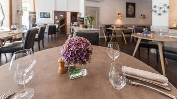 A dining area with round tables, each set with wine glasses, cutlery, and a centerpiece of purple flowers.