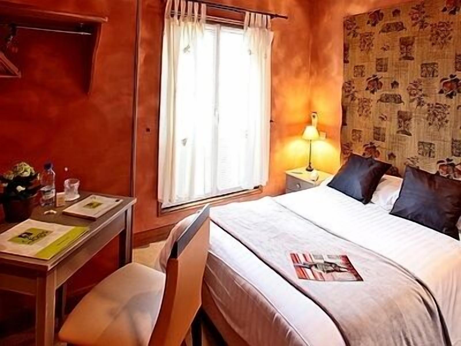 A hotel room with a bed, a desk, a chair, a lamp, and a window with curtains.