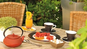 Una mesa con tetera, tazas, vaso de jugo de naranja, plato de fresas y un cuenco de terrones de azúcar.