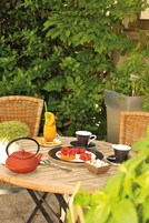Une table dressée avec une théière, des tasses, un verre de jus d’orange, une assiette de fraises et un bol de morceaux de sucre.