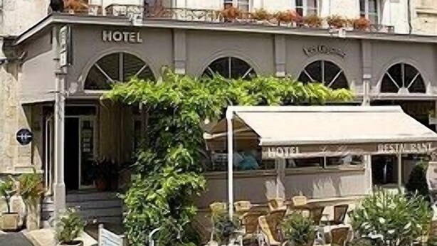Un hotel con fachada clásica, varios balcones con plantas y una zona de estar al aire libre cubierta.