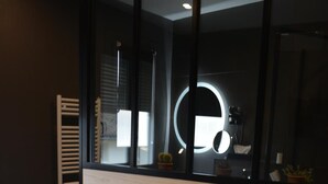 Una habitación de hotel moderna con una cama grande, dos almohadas naranjas, un cabecero azul y un espejo grande con luz circular.