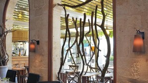 Un restaurante con paredes de piedra, ventanas arqueadas y una decoración con rama de árbol en el centro. Las mesas están dispuestas con copas de vino, platos y cubiertos.