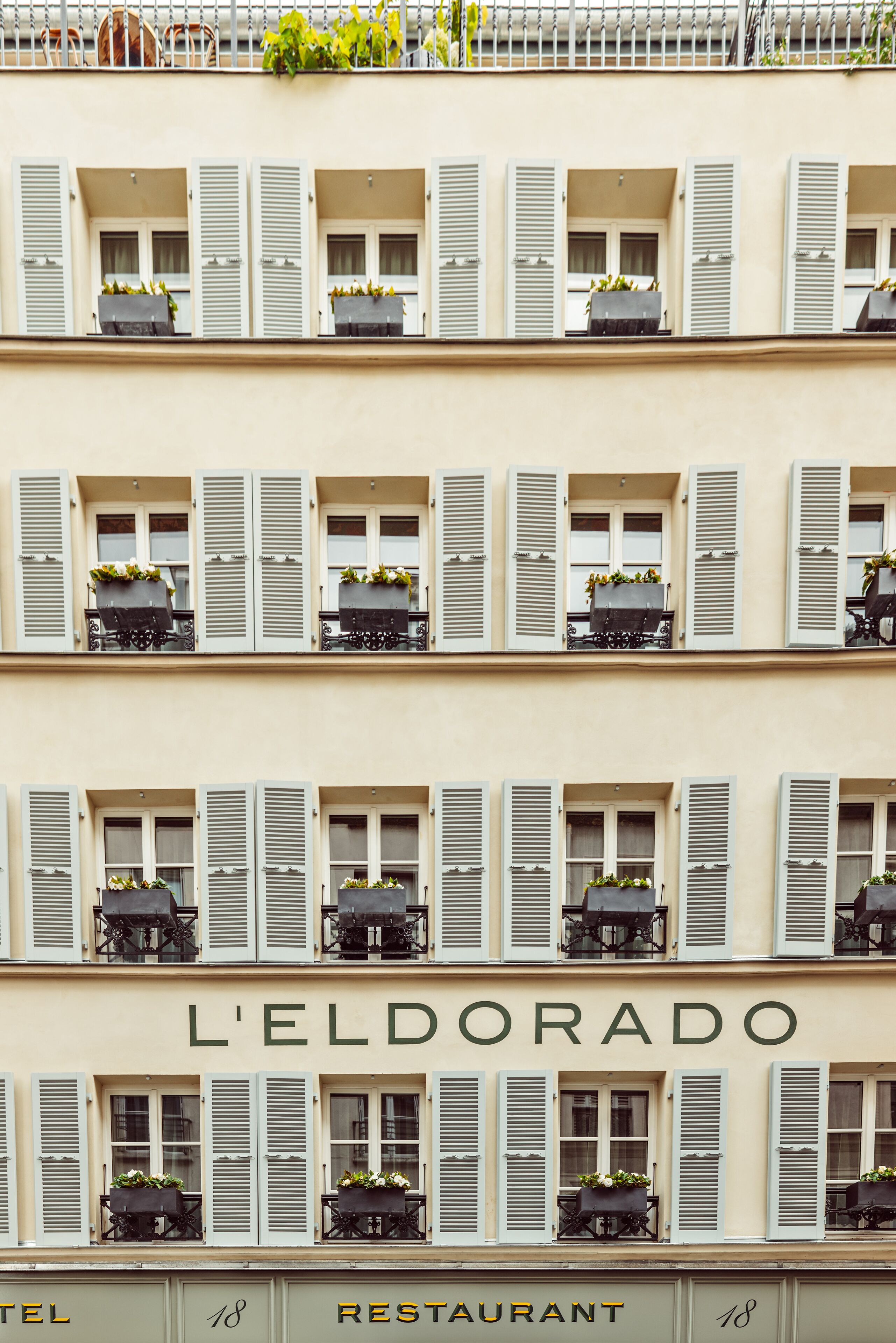 Un edificio de varios pisos con balcones, cada uno con una planta en maceta. Se muestra el nombre "L'ELDORADO" en grande.