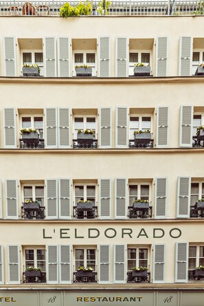 Un edificio de varios pisos con balcones, cada uno con una planta en maceta. Se muestra el nombre "L'ELDORADO" en grande.
