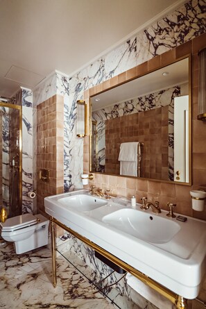 A luxurious bathroom with marble walls, a large mirror, dual sinks, and a gold-framed vanity. - Hôtel Eldorado Paris (Paris)