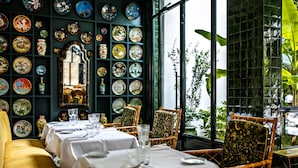 A dining area with tables set for service, a wall of decorative plates, and a view of greenery through a window. - Hôtel Eldorado Paris (Paris)