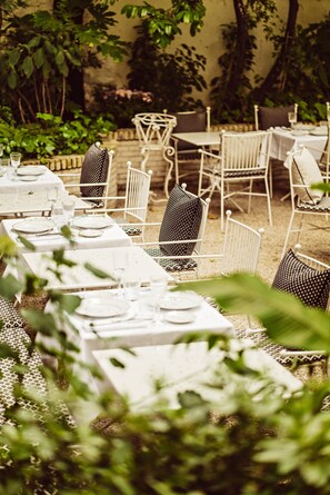 An outdoor dining area with white tables and chairs, surrounded by greenery. - Hôtel Eldorado Paris (Paris)