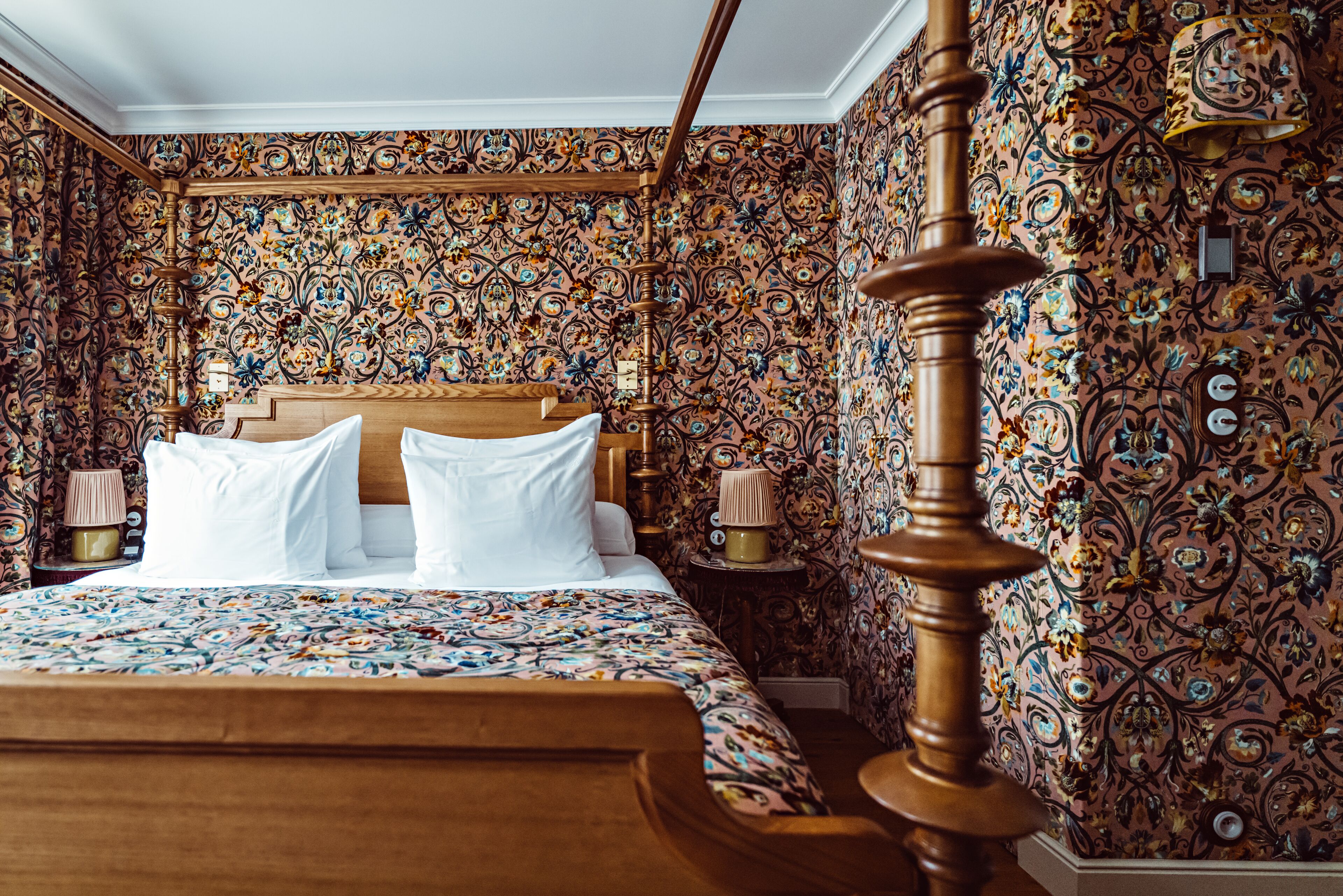 A bedroom with a wooden bed, ornate wallpaper, and a classic four-poster bed frame.