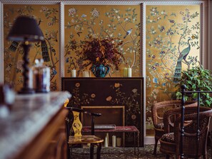 A room with a fireplace, a vase with dried flowers, and wicker furniture. - Hôtel Eldorado Paris (Paris)
