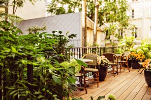 A wooden deck with outdoor furniture, surrounded by lush greenery and potted plants. - Hôtel Eldorado Paris (Paris)