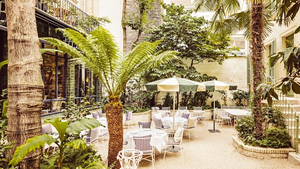 An outdoor patio area with tables and chairs, surrounded by lush greenery and palm trees. - Hôtel Eldorado Paris (Paris)