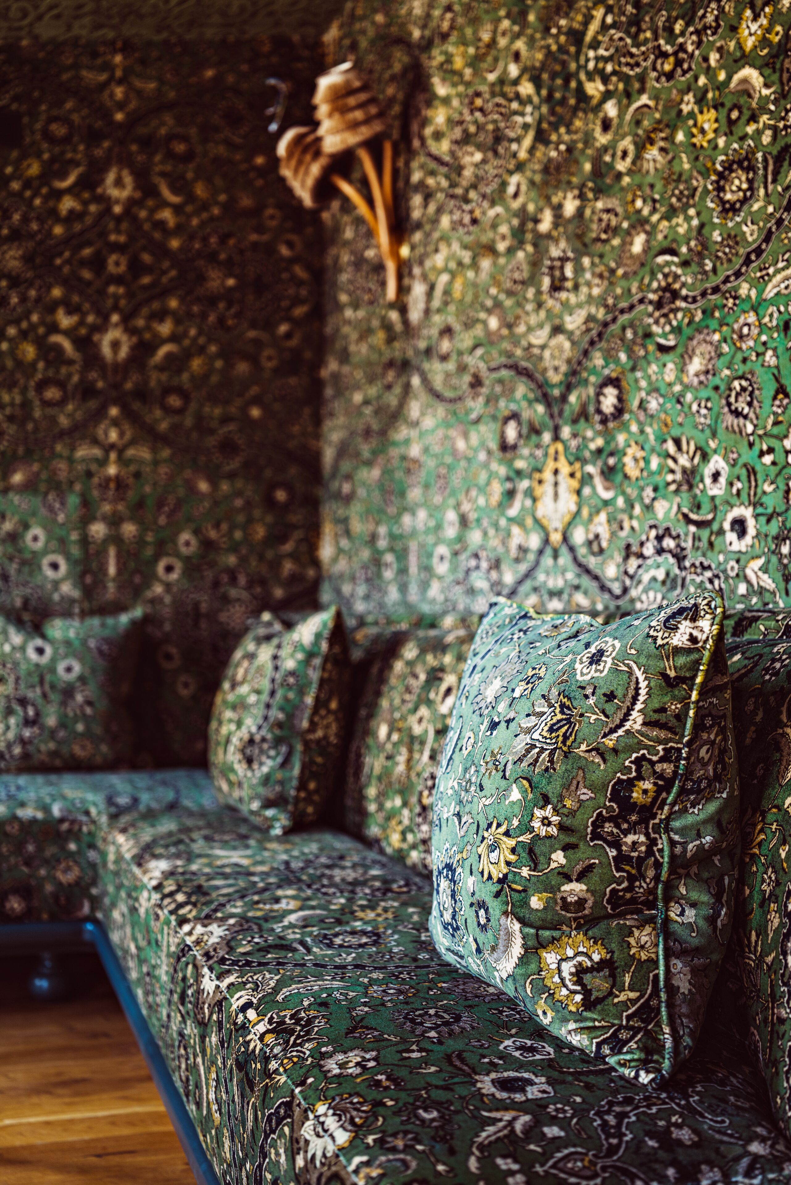 A sofa with a detailed floral pattern, a wooden sculpture, and a patterned wall.