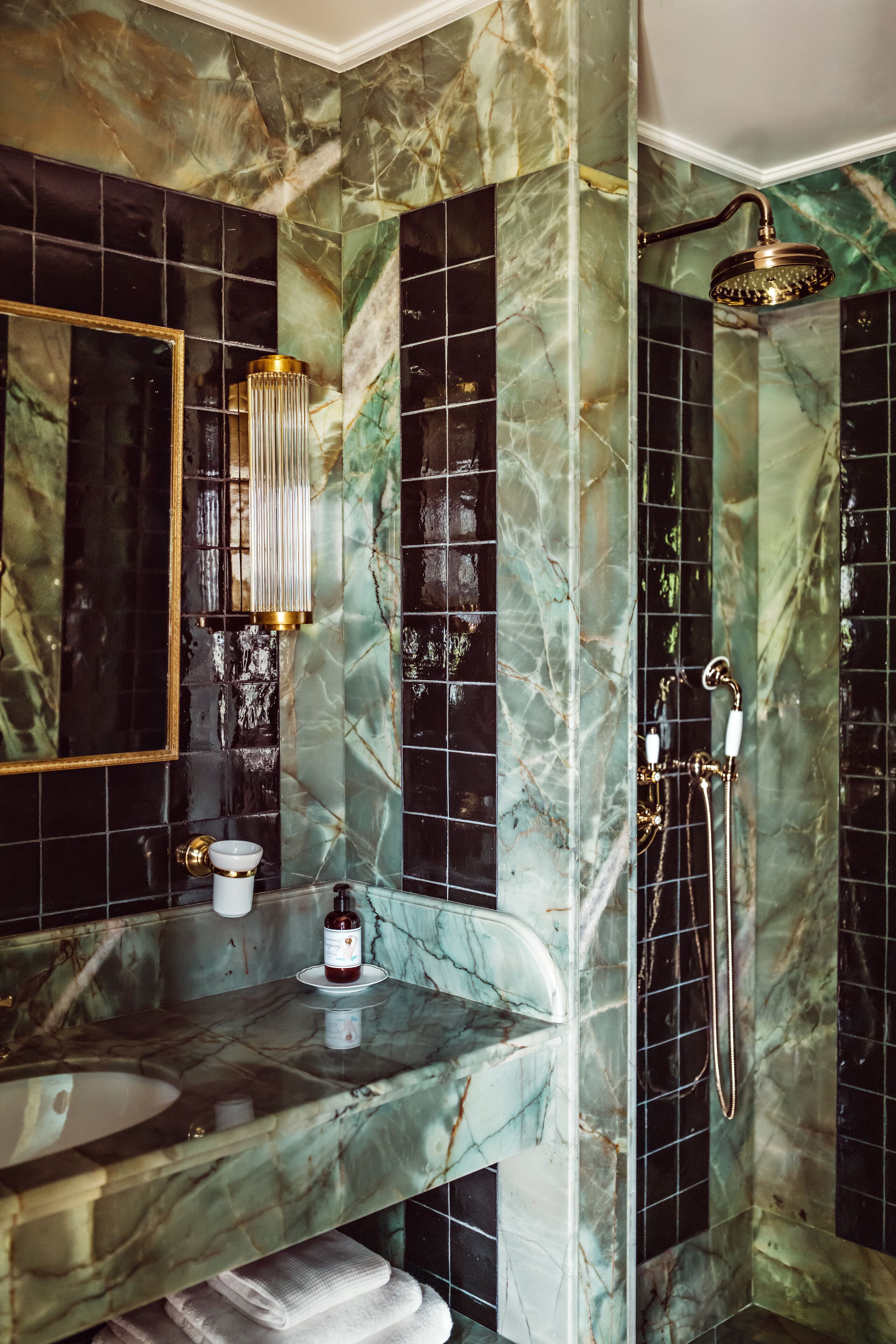 A bathroom with a marble sink, a gold-framed mirror, and a shower with a gold showerhead.