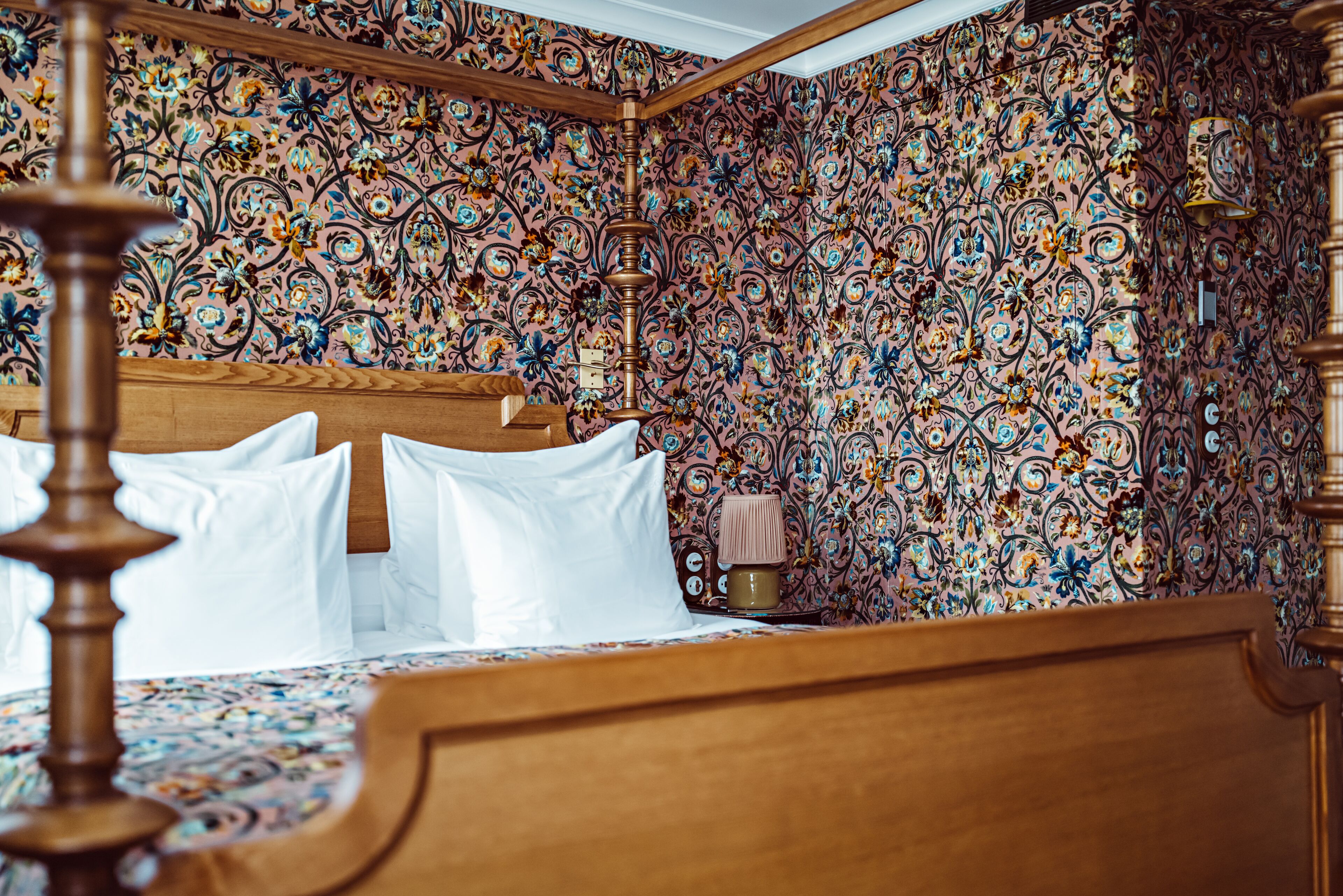 Ein Schlafzimmer mit einem hölzernen Bett, Blumenpapier und einem Nachttisch mit Lampe.