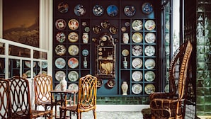 A room with a wall of decorative plates, wicker furniture, and a patterned carpet. - Hôtel Eldorado Paris (Paris)