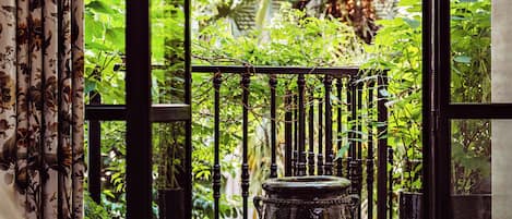 A balcony with a view of lush greenery, a large pot, and a patterned rug.