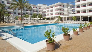 Une piscine entourée de chaises longues et agrémentée de plantes en pot, le tout bordé d’un bâtiment blanc doté de balcons.