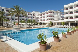Una piscina con sillones de descanso y plantas en macetas, rodeada por un edificio blanco con balcones.