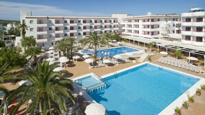 Un hôtel doté d’une grande piscine, de chaises longues, de parasols et de palmiers.