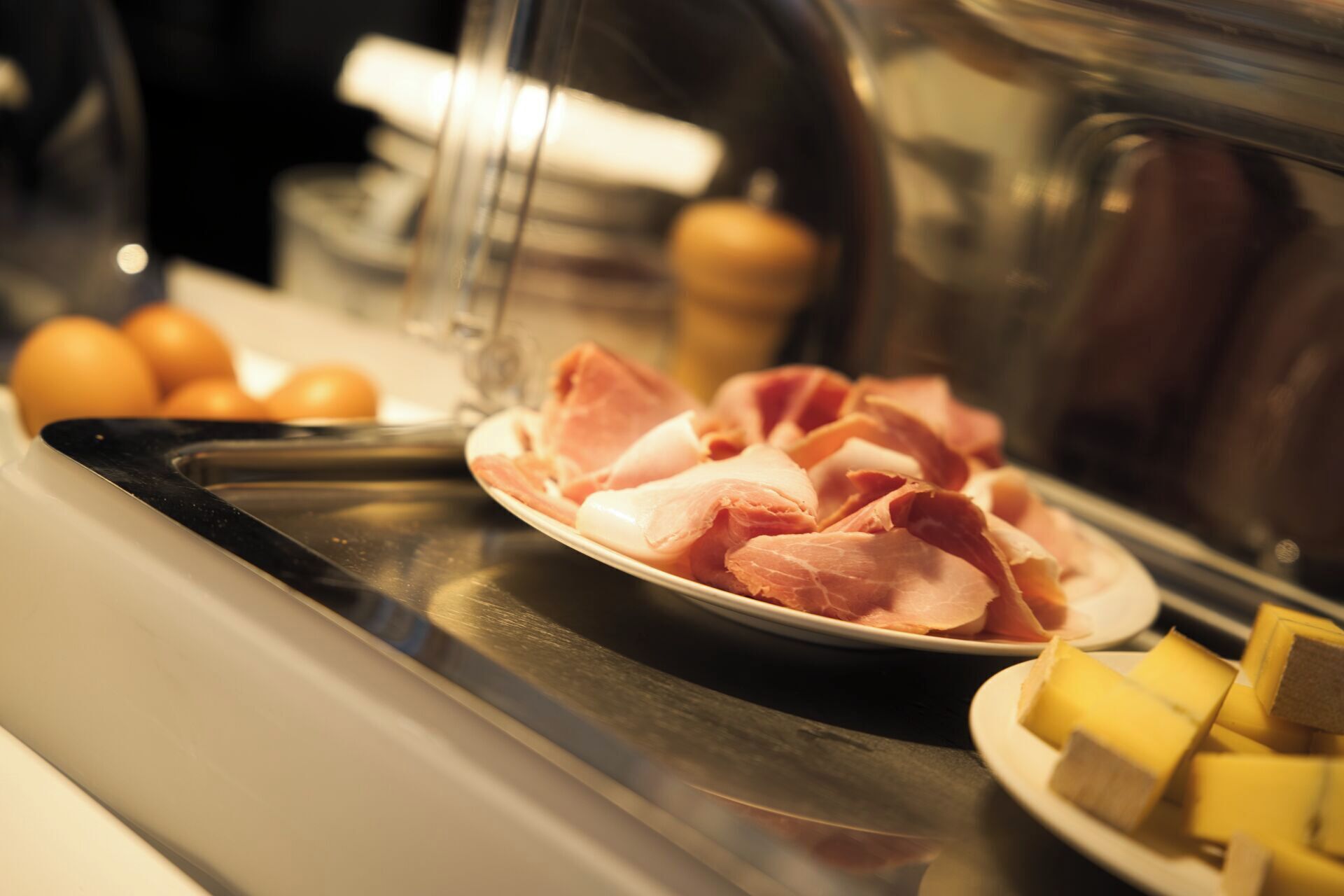 A buffet with a plate of sliced ham and cheese, and a plate of oranges.