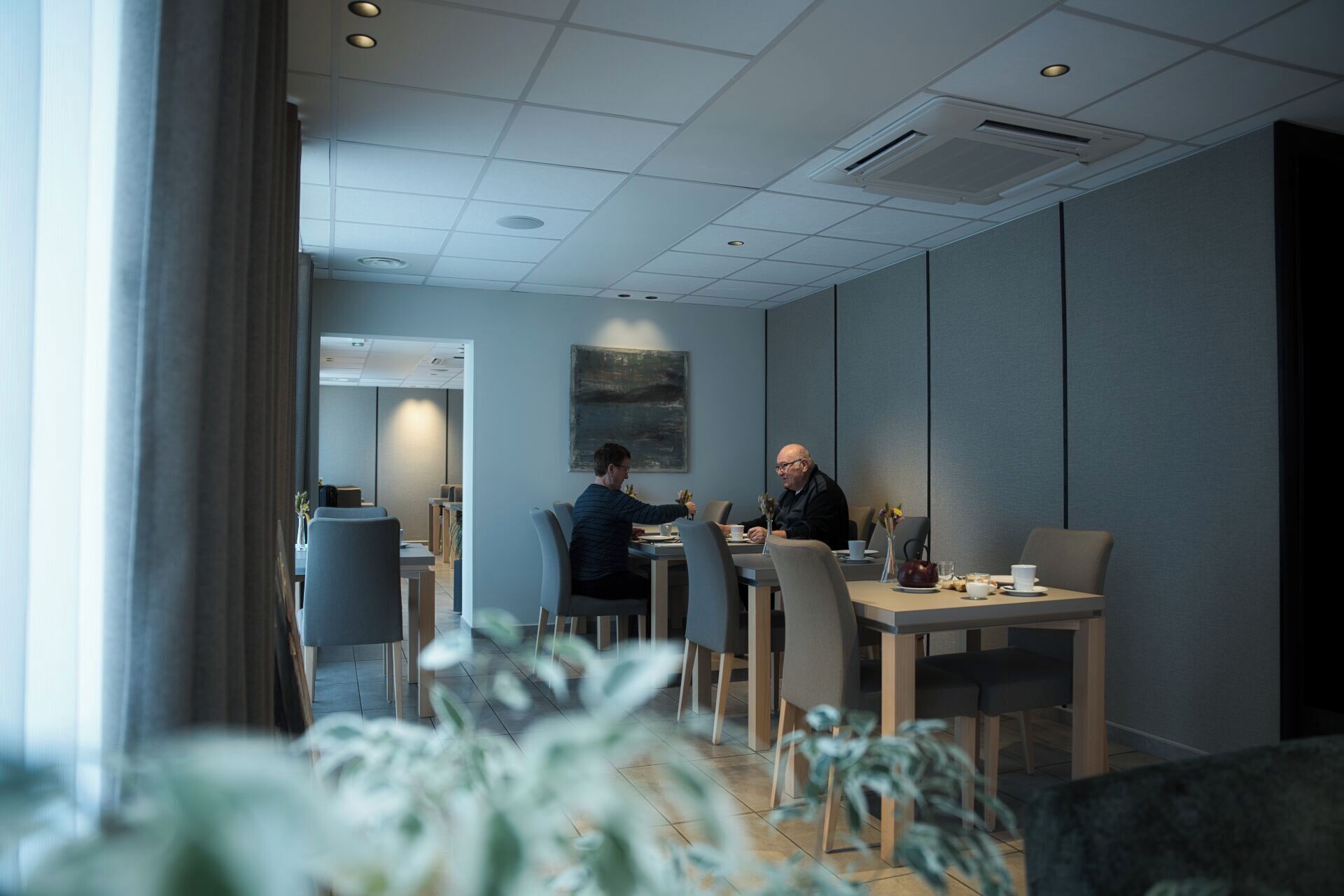 A modern meeting room with a long table, chairs, and a painting on the wall.
