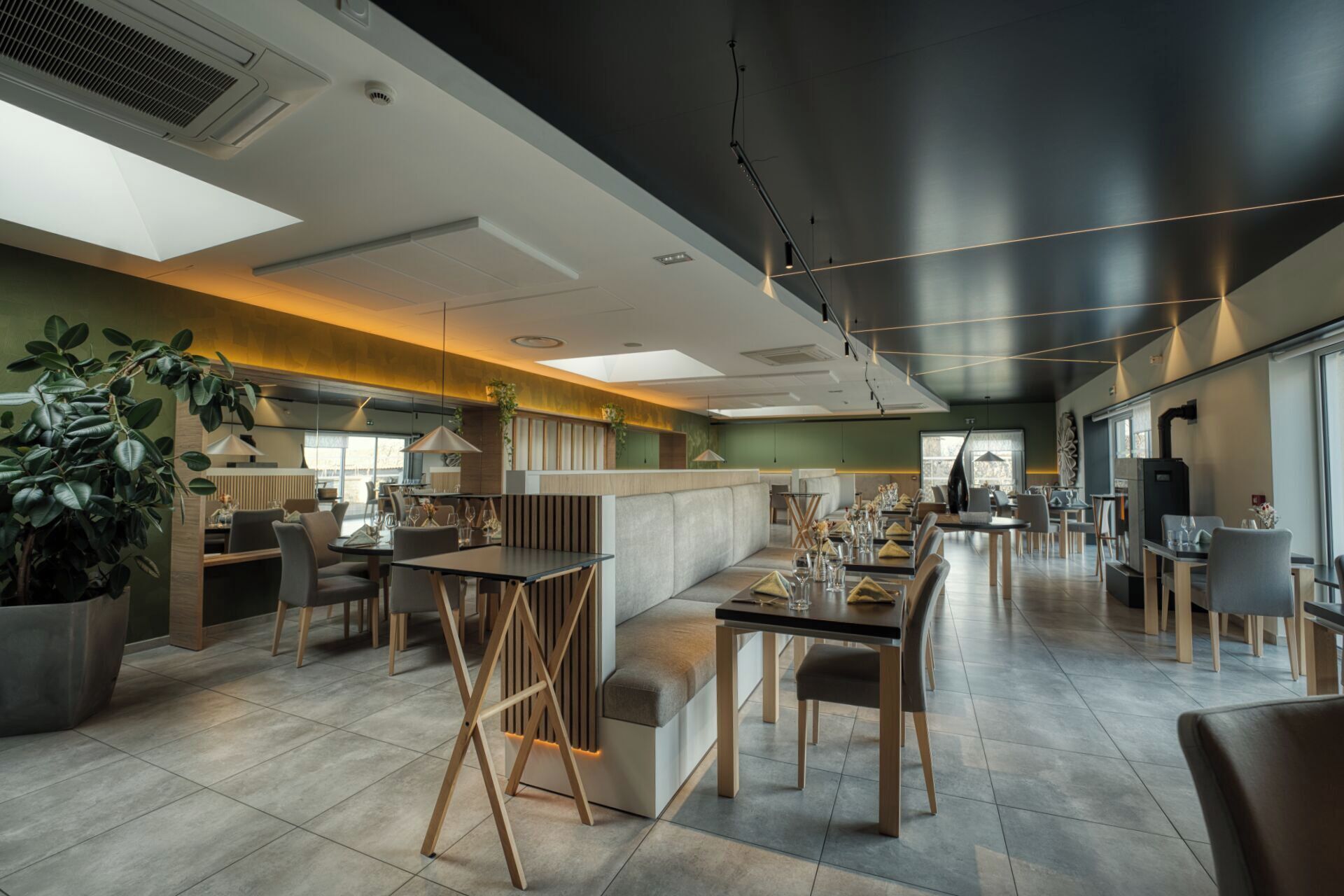 A modern restaurant interior with high ceilings, recessed lighting, and a mix of seating arrangements including tables and booths.
