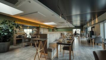 A modern restaurant interior with high ceilings, recessed lighting, and a mix of seating arrangements including tables and booths.