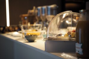A buffet setup with a glass dome covering a food display, a bowl, and a bottle on a counter. - Hotel A la 12 (Delme)